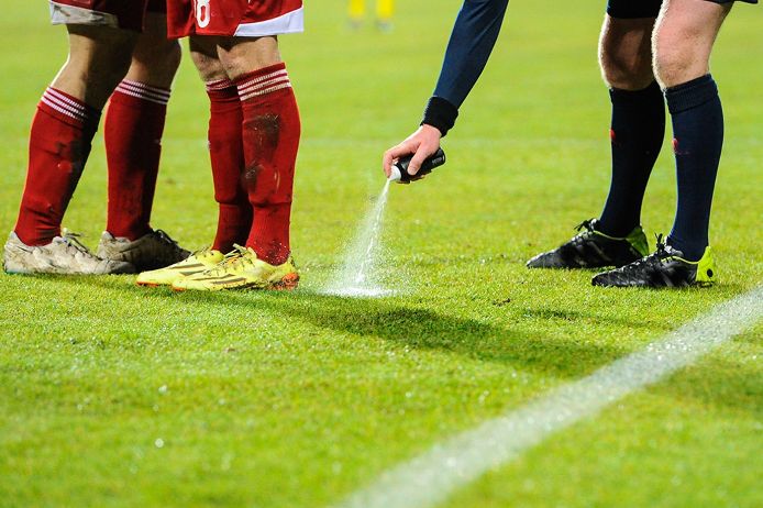 Ein Schiedsrichter sprüht mit einem Freistoßspray den Mauerabstand auf einem Fussballfeld